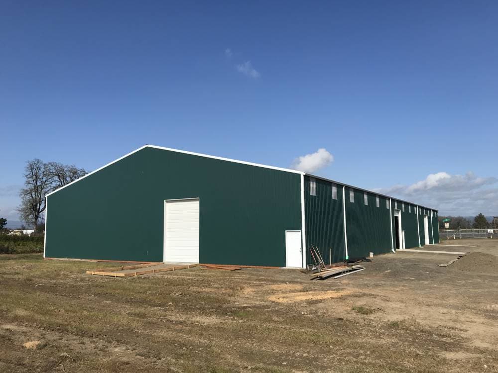 Green steel-sided agricultural warehouse with white trim and a large clear-span gable end, built by Miner Pole Buildings