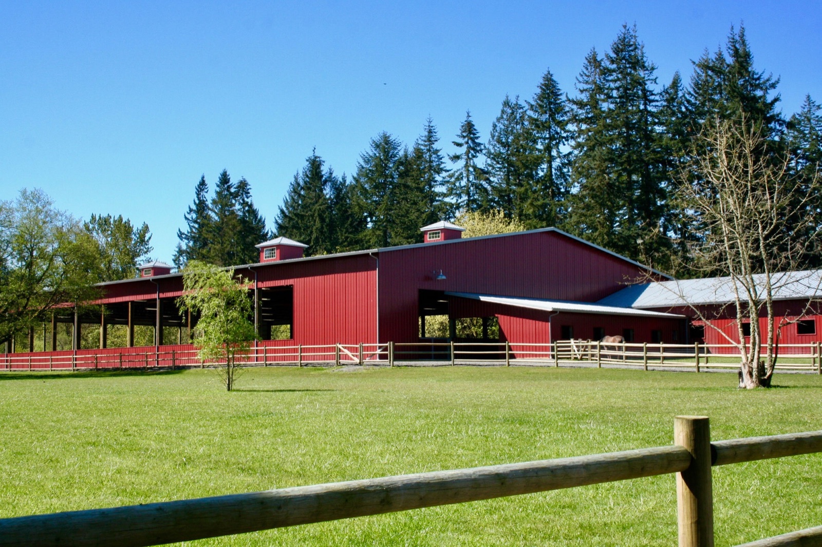 Red post-frame agricultural barn with a covered lean-to on green pasture, built by Miner Pole Buildings