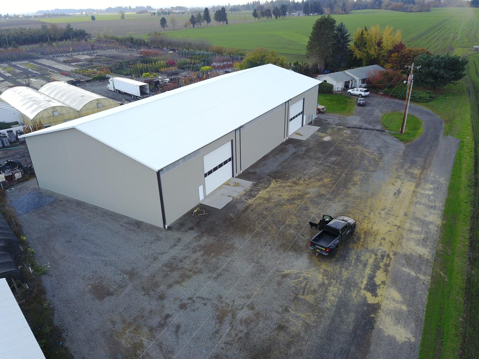 Aerial view of a white multi-bay commercial pole building with roll-up doors and a paved equipment yard, built by Miner Pole Buildings