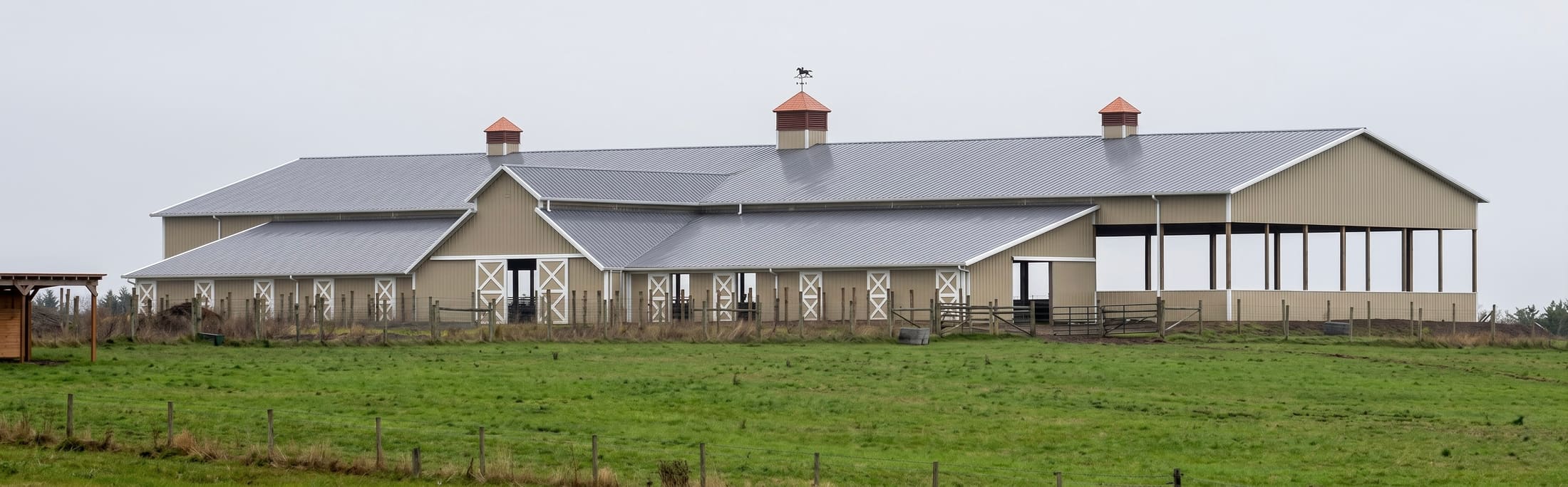 Long covered riding arena with open side wings on an Oregon hillside, built by Miner Pole Buildings