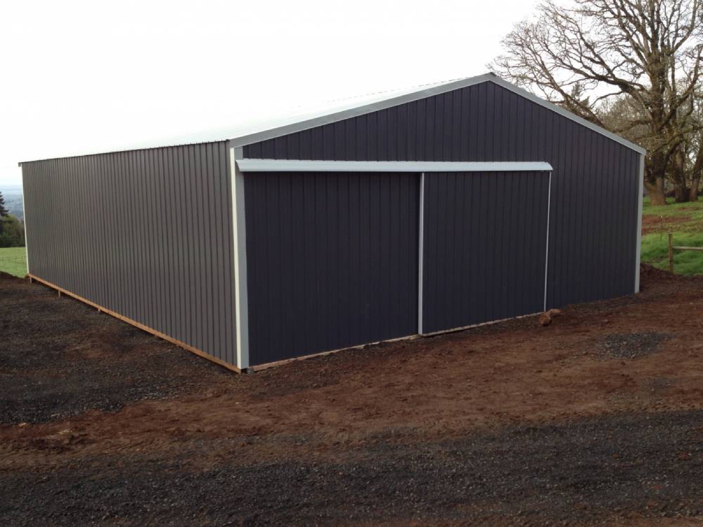 Charcoal post-frame shop with tan trim on a hilltop, built by Miner Pole Buildings