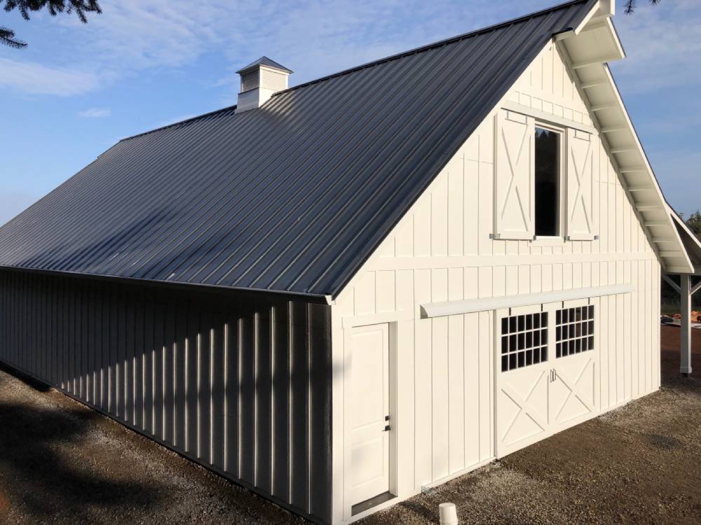 White board-and-batten barn with a black metal roof and cupola, built by Miner Pole Buildings