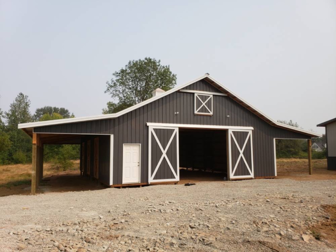 Charcoal and white barn with X-brace doors and lean-tos, built by Miner Pole Buildings