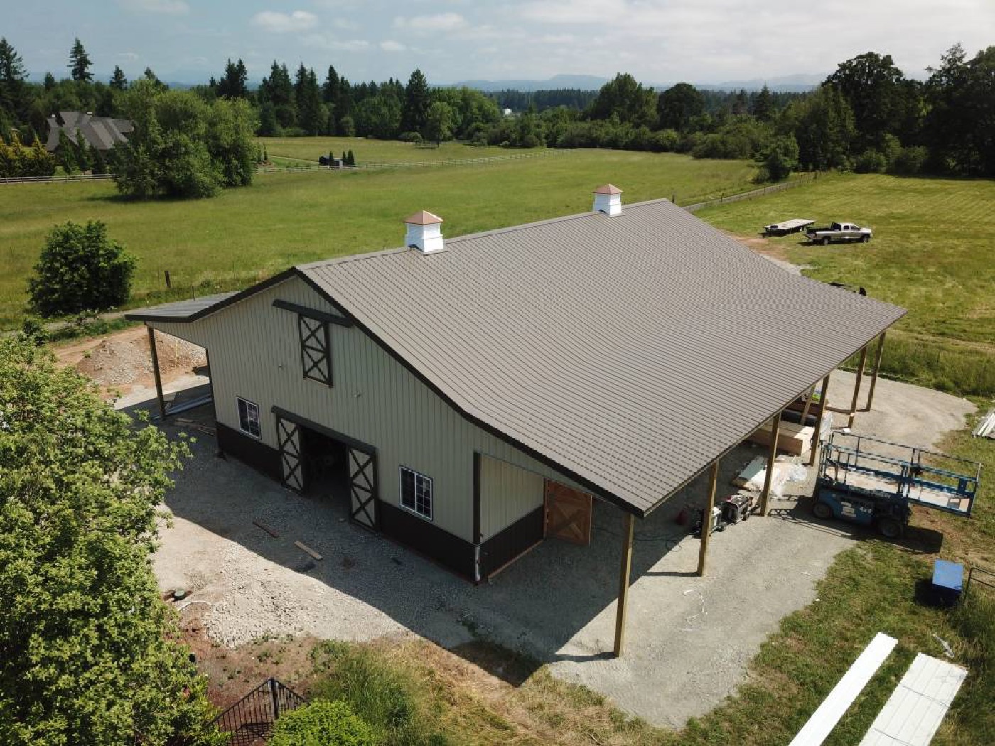 Aerial view of a tan and black barn with cupolas over pasture, built by Miner Pole Buildings