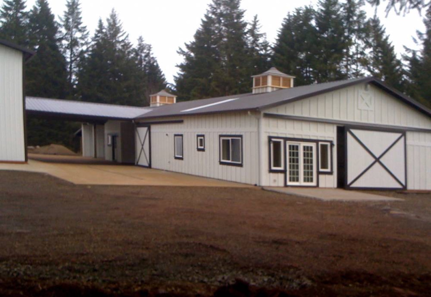 White board-and-batten barn with cupolas, X-doors, and a breezeway, built by Miner Pole Buildings
