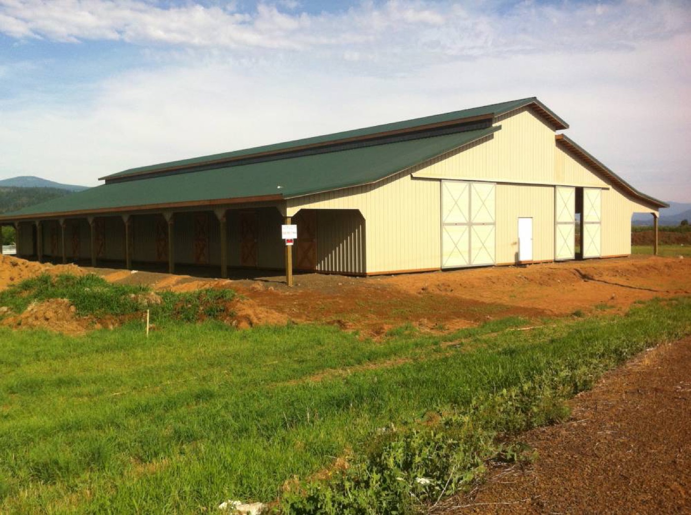 Tan barn with a green roof and a covered lean-to, built by Miner Pole Buildings