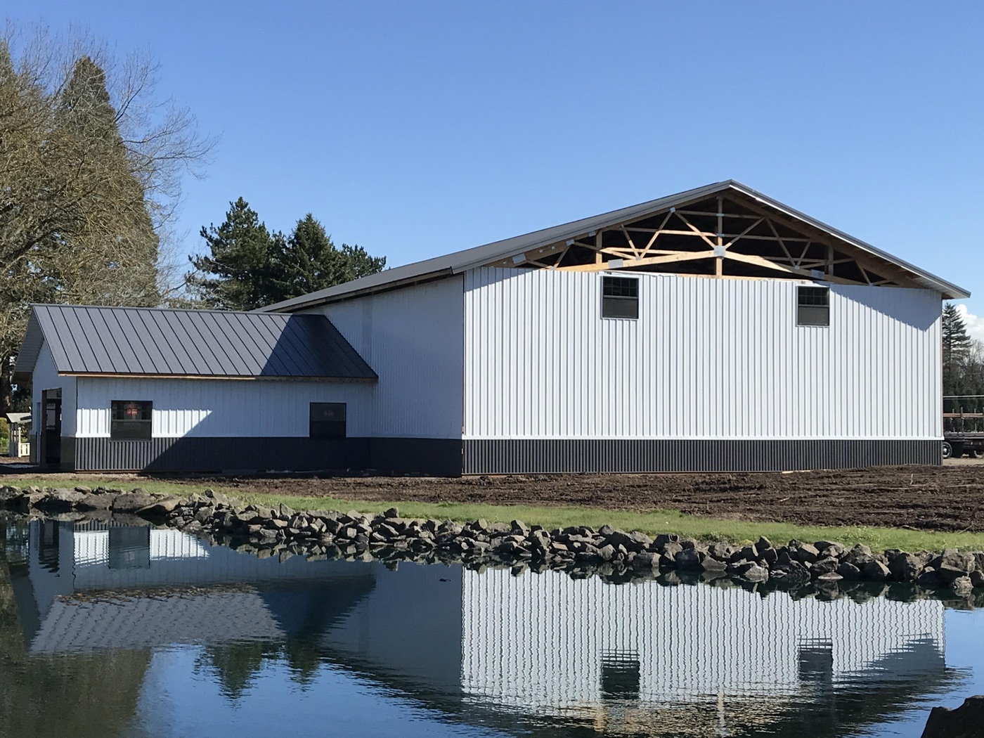 White barn with brown wainscot mirrored in a pond, built by Miner Pole Buildings