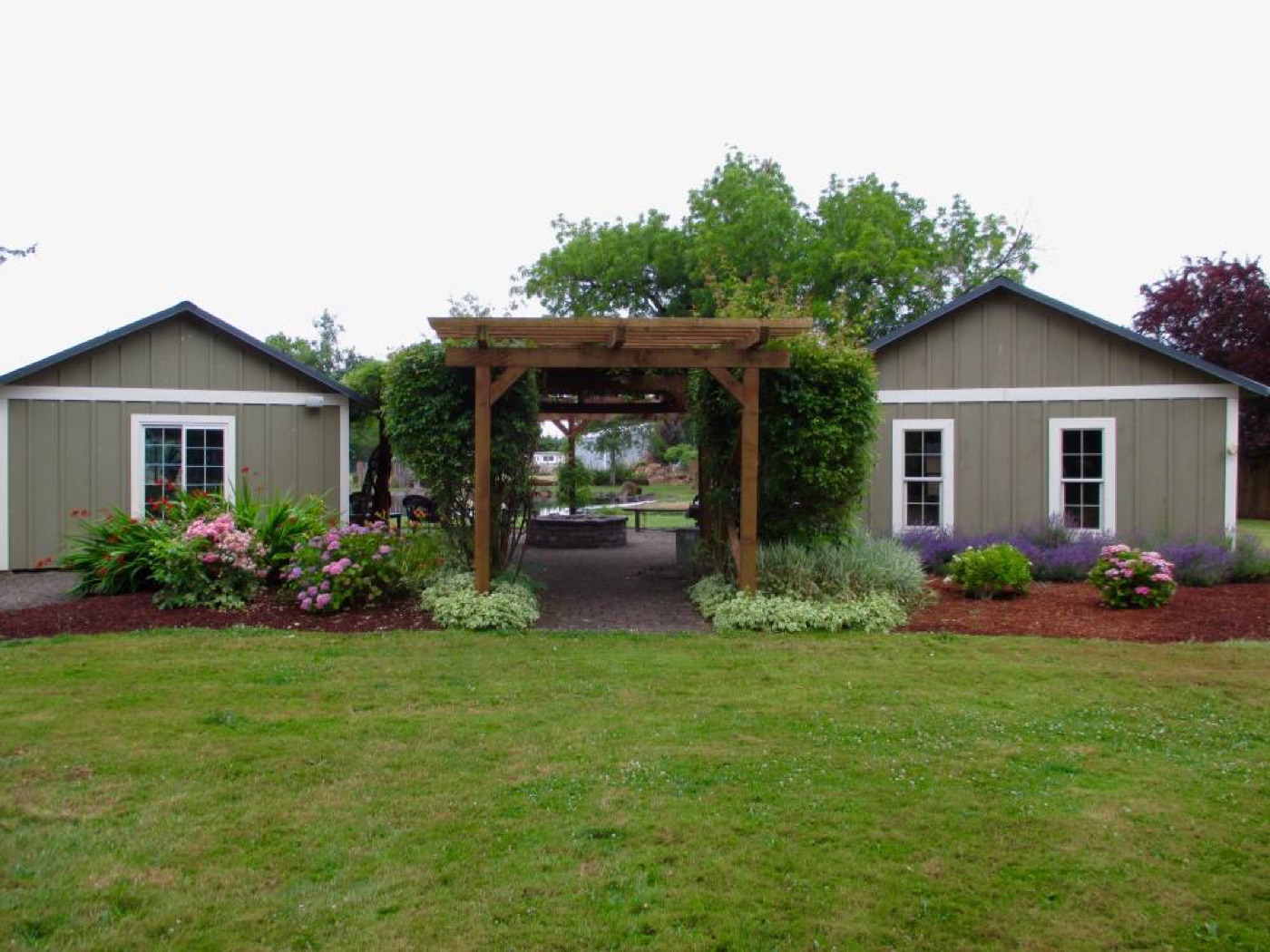 Twin sage storage buildings flanking a garden pergola, built by Miner Pole Buildings