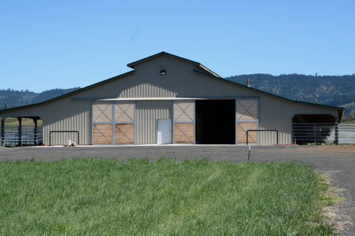 Tan monitor horse barn with green trim and X-brace doors against a mountain backdrop, built by Miner Pole Buildings