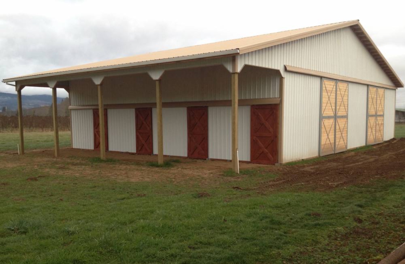 Cream stall barn with red dutch doors beside a vineyard, built by Miner Pole Buildings