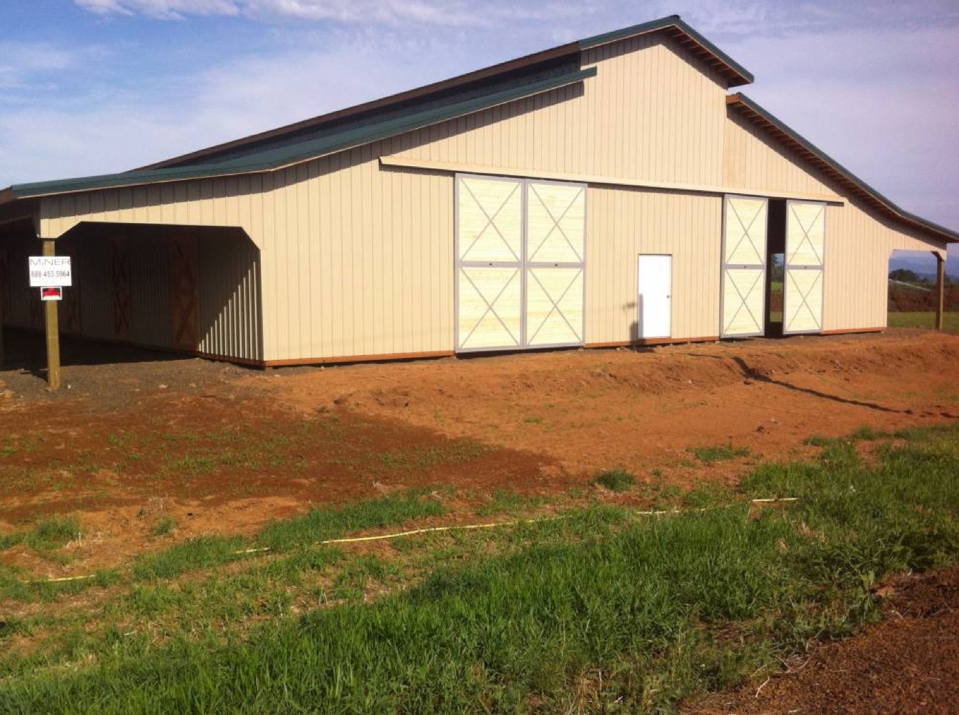 Tan stall barn with a green roof and white X-cross doors, built by Miner Pole Buildings