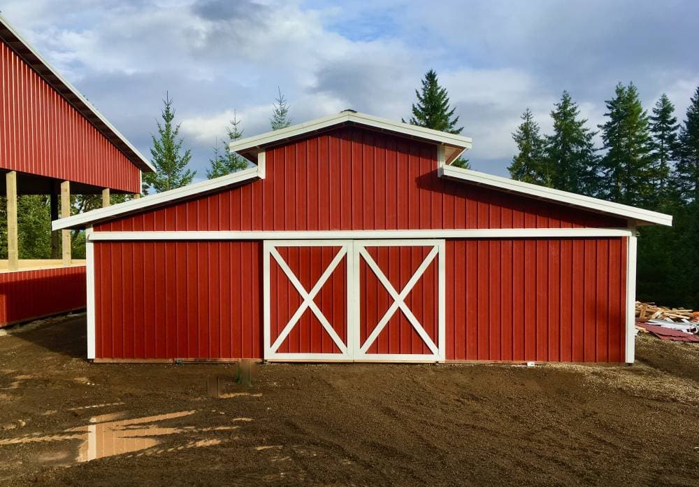 Red post-frame barn with white sliding X-doors and a matching lean-to on a gravel pad, built by Miner Pole Buildings